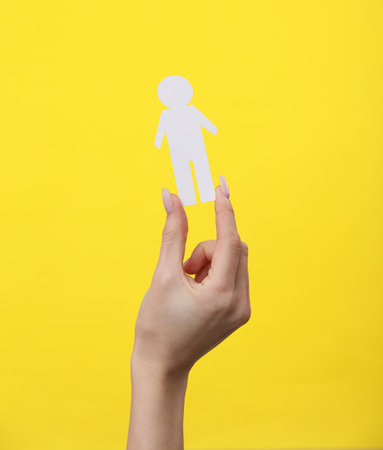 Woman's hand holds a paper cut man on yellow backgroundの写真素材