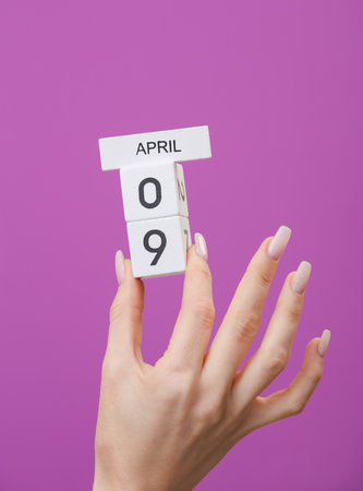 Block calendar with date april 09 in female hand on purple background