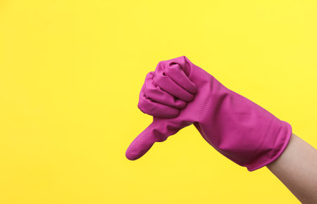 Hand in purple rubber cleaning glove shows thumbs down on a yellow background. House cleaning and housekeeping conceptの写真素材