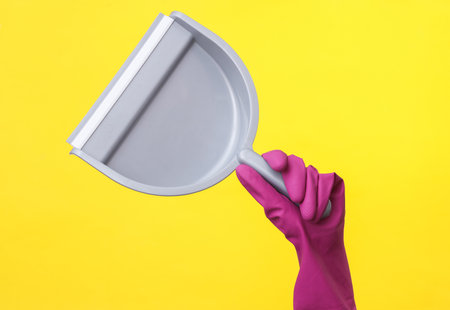 Hand in purple rubber cleaning glove holding scoop on a yellow background. House cleaning and housekeeping conceptの写真素材