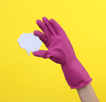 Hand in purple rubber cleaning glove holding speech bubble on a yellow background. House cleaning...