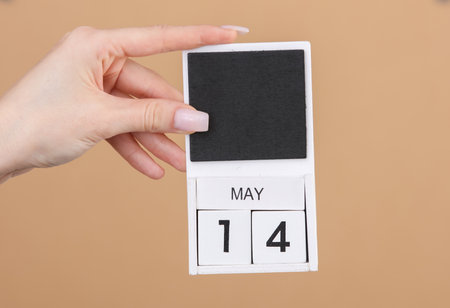 Block calendar with date may 14 in female hand on brown backgroundの写真素材