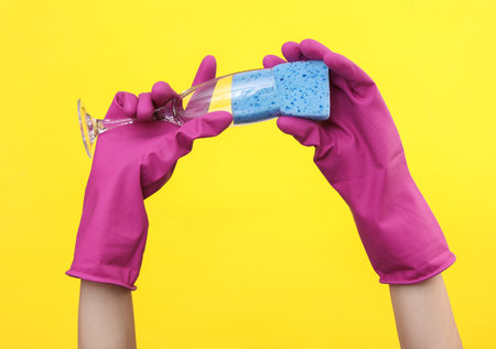 Hands in rubber gloves wash a glass on a yellow backgroundの写真素材