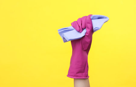 Hand in purple rubber cleaning glove holding rag on yellow background. House cleaning and housekeeping conceptの写真素材