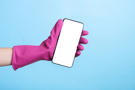 Hand in purple rubber cleaning glove holding smartphone with white screen on a blue background....