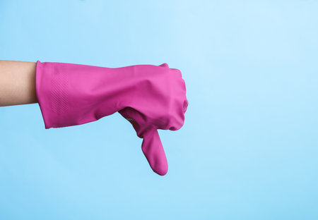 Hand in purple rubber cleaning glove shows thumbs down on a blue background. House cleaning and housekeeping conceptの写真素材