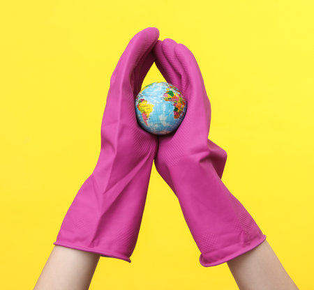 Hands in purple rubber cleaning gloves holding globe on a yellow background. House cleaning and housekeeping concept
