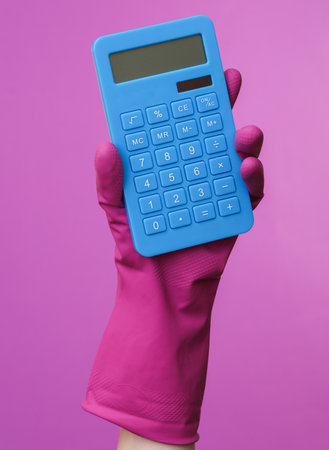 Hand in purple rubber cleaning glove holding calculator on purple background. House cleaning and housekeeping conceptの写真素材