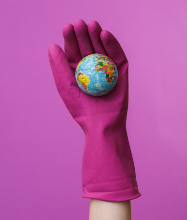 Hand in purple rubber cleaning glove holding globe on purple background. House cleaning and...