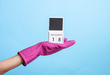 Hand in purple rubber cleaning glove holding calendar with date september 18 on blue background. world cleanliness day. House cleaning and housekeeping conceptの写真素材