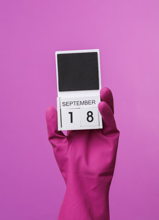 Hand in purple rubber cleaning glove holding calendar with date september 18 on purple background. world cleanliness day. House cleaning and housekeeping conceptの写真素材