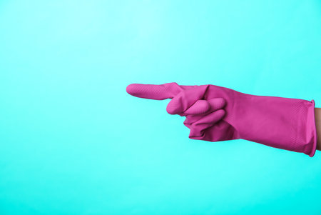 Hand in purple rubber cleaning glove points to the side on blue background. House cleaning and housekeeping concept. copy spaceの写真素材