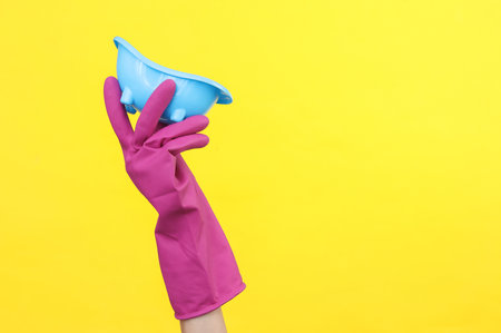 Hand in purple rubber cleaning glove holding toy bath on a yellow background.の写真素材