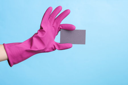 Hands in purple rubber cleaning gloves holding gray business card on blue background.の写真素材