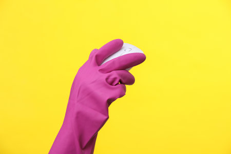 Hand in purple rubber cleaning glove holding pc mouse on a yellow background.の写真素材