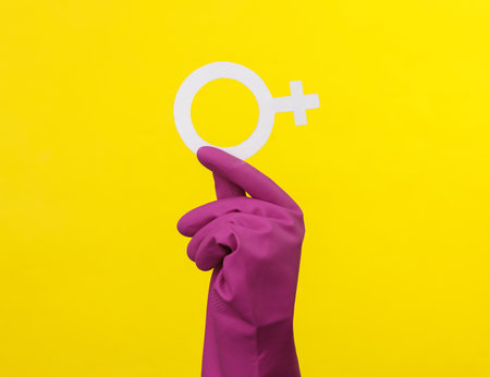 Feminism. Women's power. Hand in rubber cleaning glove holds a female gender symbol venev on a yellow backgroundの写真素材