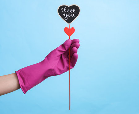 Hand in purple rubber cleaning glove holding valentine on blue background.の写真素材