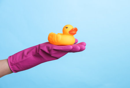 Hand in purple rubber cleaning glove holding rubber duck on a blue background. House cleaning and housekeeping conceptの写真素材
