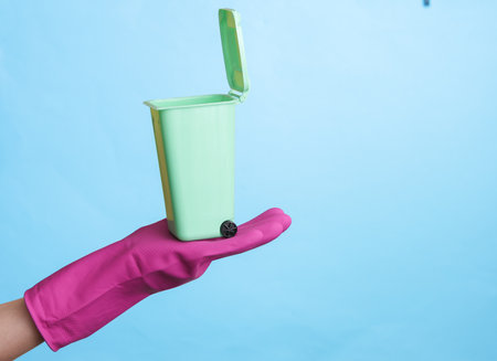 Hand in purple rubber cleaning glove with mini trash can on blue background.の写真素材