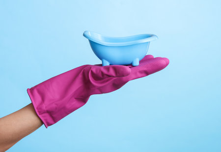 Hand in purple rubber cleaning glove holding toy bath on blue background.の写真素材