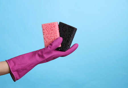 Hand in purple rubber cleaning glove holding sponges on blue background. House cleaning and housekeeping conceptの写真素材