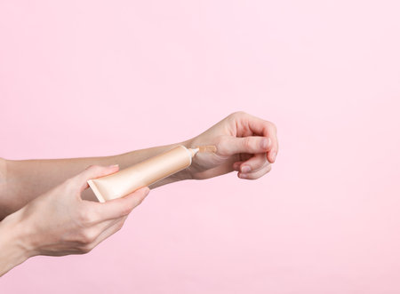 Female hands holding a tube of foundation on pink backgroundの写真素材