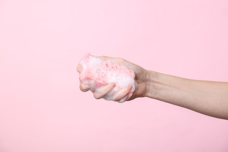 Woman's hand holds a sponge in foam on a pink background. cleaning conceptの写真素材