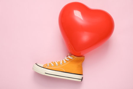 Red heart-shaped air balloon with retro sneaker on pink background. Valentine's Day. creative layoutの写真素材