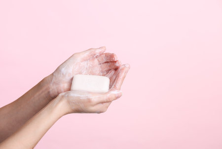 Female hands holding foaming soap on a pink background. Hygiene, clean handsの写真素材