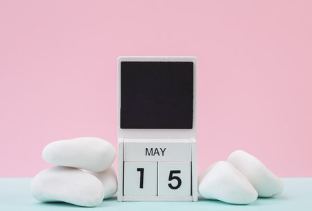 Block wooden calendar with the date may 15 and white pebbles on pastel background.の写真素材