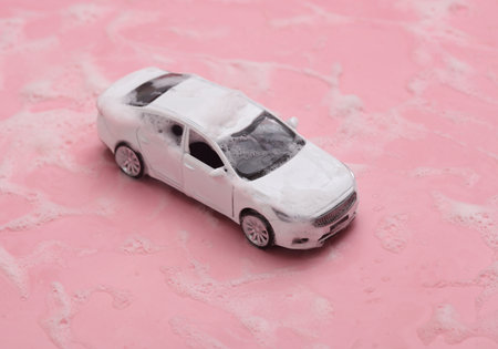 Toy car in foam on a pink background. car wash