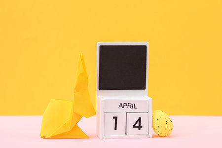 happy easter. Calendar with date april 14 and easter rabbit with eggs on yellow backgroundの写真素材
