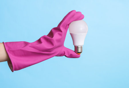 Hand in purple rubber cleaning glove holding led light bulb on a blue background. House cleaning and housekeeping conceptの写真素材