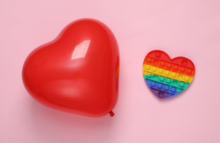 Red heart-shaped air balloon with pop it antistress toy on a pink background. Valentine's Dayの写真素材