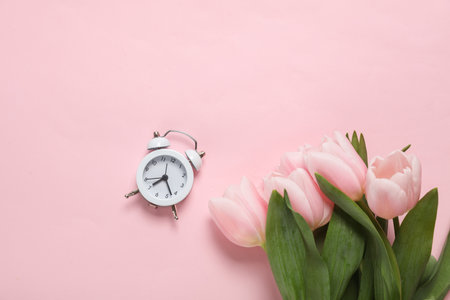 Bouquet of pink tulips with an alarm clock on a pink background. holiday background. top view