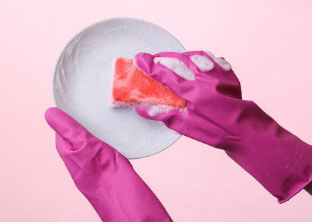 Hands in rubber gloves wash plate on pink backgroundの写真素材