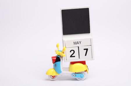 Block wooden calendar with the date may 27 on toy moped, white background
