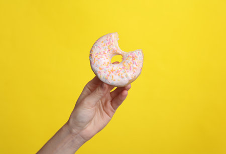 Woman's hand holding a bitten donut on a yellow backgroundの写真素材