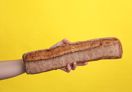 Woman's hand holding rye baguette on yellow backgroundの写真素材