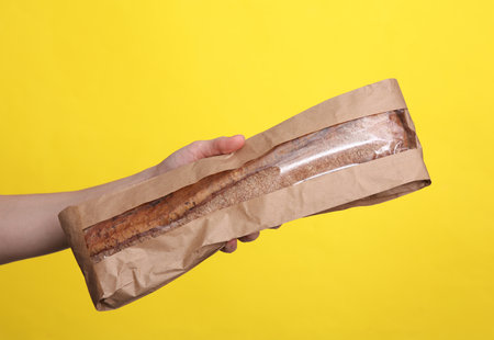 Woman's hand holding rye baguette on yellow backgroundの写真素材