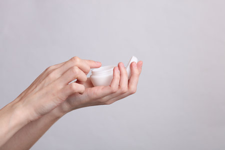 Woman's hands holding white jar of cream on gray backgroundの写真素材