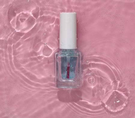 Nail polish bottle in pink water with shadows. top viewの写真素材