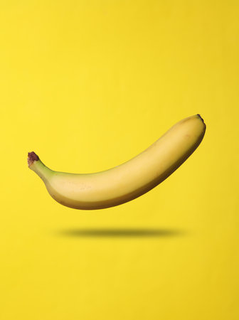 Ripe banana levitates on yellow background with shadowの写真素材