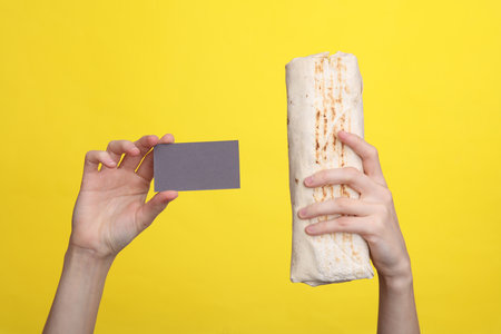 Female hands holding shawarma and business card on a yellow backgroundの写真素材