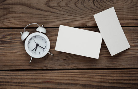 White Blank business cards for branding and alarm clock on wooden table. Creative Mockup for...
