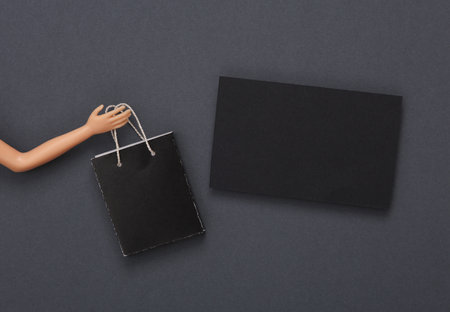Doll hand holds a shopping bag and business card on gray background. creative layoutの写真素材