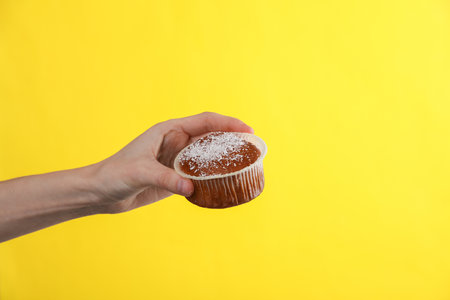 appetizing cupcake or muffin in female hand on yellow backgroundの写真素材