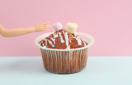 Appetizing muffin with puppet hand on blue-pink pastel background. food concept