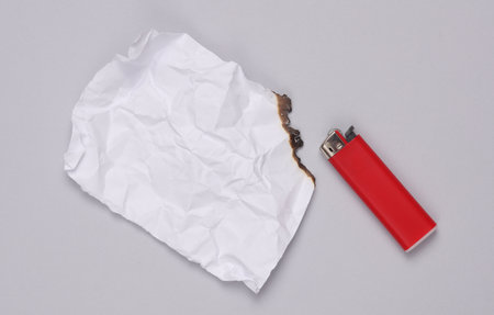Burnt sheet of paper with a lighter on a gray background