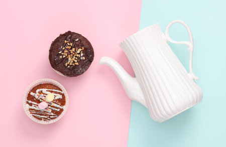 Ceramic teapot with cupcakes on a blue-pink pastel background. top viewの写真素材